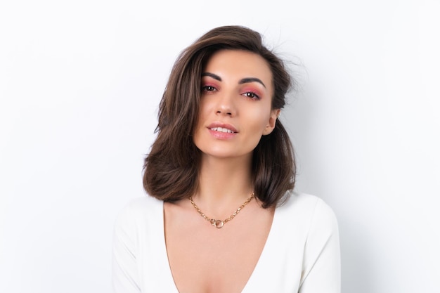 Mujer joven en una cadena de oro de vestido de cóctel y maquillaje rosa primavera brillante sobre un fondo blanco Sonríe alegremente