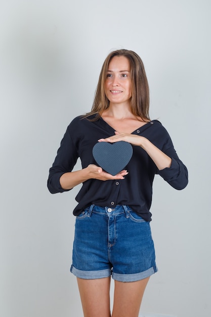 Mujer joven con caja de regalo en camisa negra, pantalones cortos de jeans