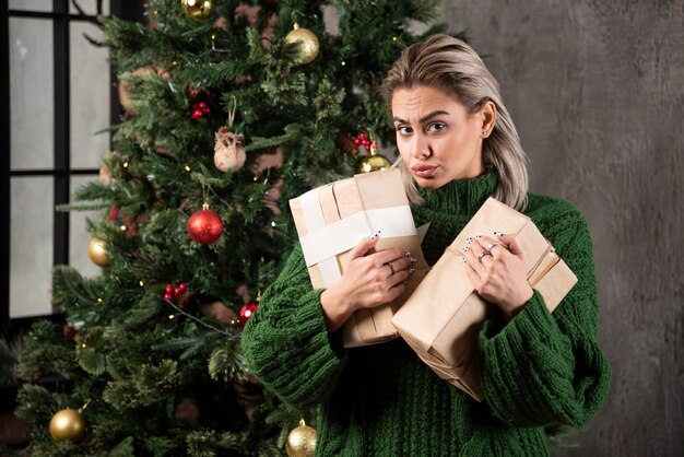 Mujer joven con caja de regalo cerca de un árbol de Navidad