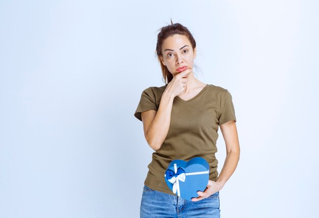 Mujer joven con una caja de regalo con forma de corazón azul parece insatisfecha