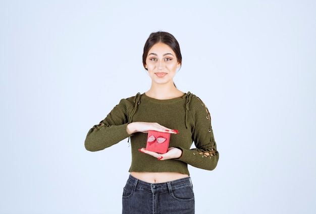 Mujer joven con caja de regalo y mirando a cámara sobre fondo blanco.