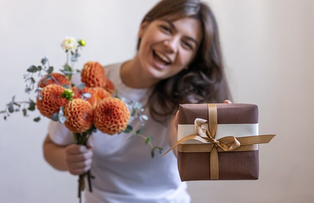 Mujer joven con una caja de regalo y un ramo de flores de crisantemo