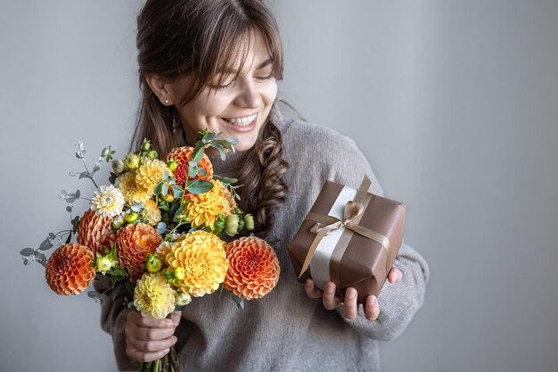 Mujer joven con una caja de regalo y un ramo de flores en las manos