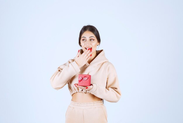 Mujer joven con una caja de regalo roja se ve feliz y sorprendida