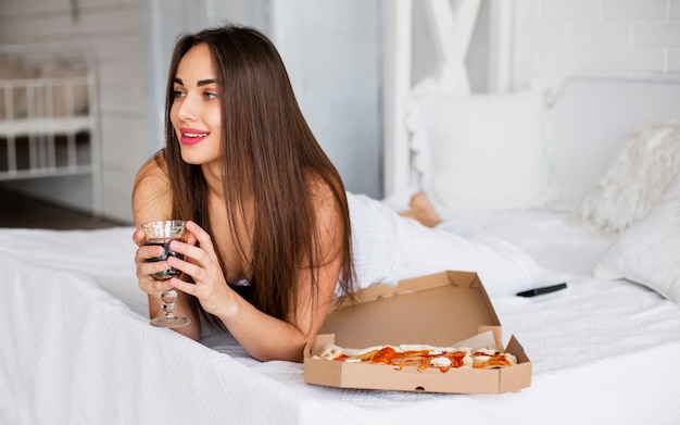 Mujer joven en la cama comiendo pizza