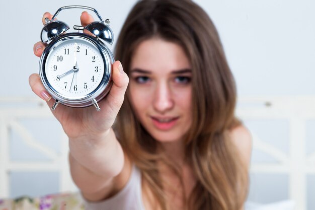 Mujer joven en la cama con reloj despertador