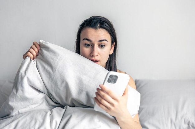 Una mujer joven en la cama con un teléfono inteligente por la mañana