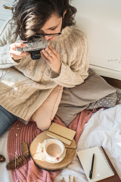 Mujer joven con cámara de fotos sentado en manta con almohadas