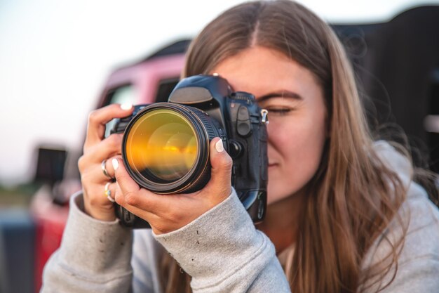 Una mujer joven con una cámara profesional toma una foto en la naturaleza.