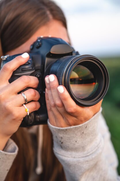 Una mujer joven con una cámara profesional toma una foto en la naturaleza.