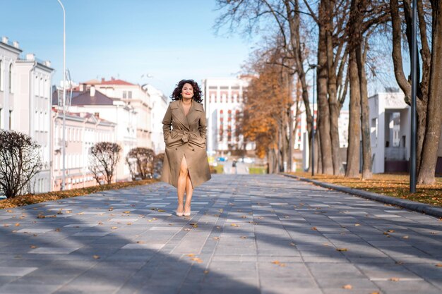 una mujer joven camina por la ciudad de otoño, una mujer de cuerpo feliz con el pelo rizado en un impermeable.