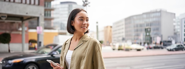 Foto gratuita mujer joven caminando por la calle de la ciudad gire hacia atrás usando el navegador de la aplicación de mapas en el teléfono inteligente sosteniendo