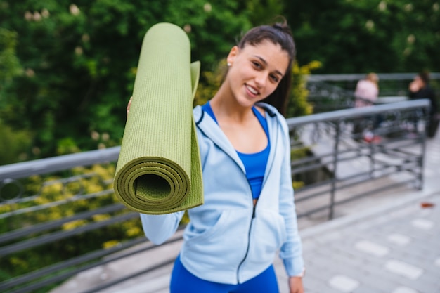 Mujer joven caminando en el parque urbano con alfombra de fitness.