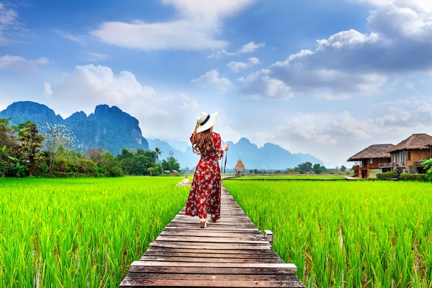 Mujer joven caminando por el sendero de madera con campo de arroz verde en Vang Vieng, Laos.