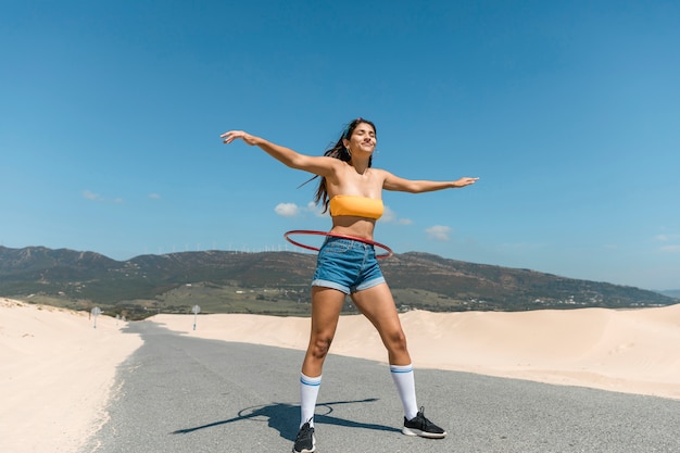 Mujer joven en el camino jugando con hula hoop