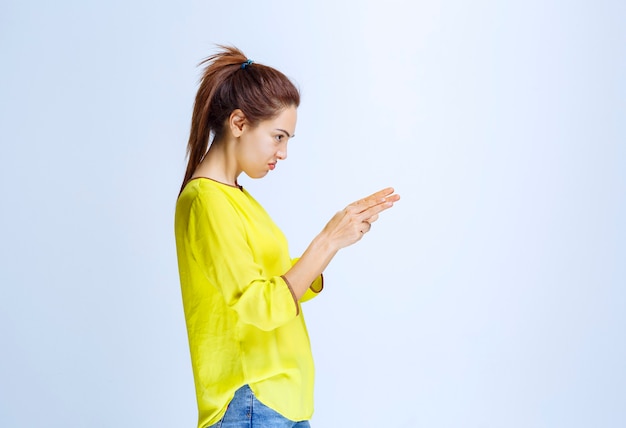 Mujer joven con camisa amarilla mostrando algo a la derecha