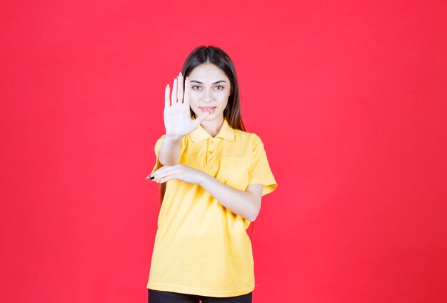 Mujer joven en camisa amarilla de pie en la pared roja y detener algo