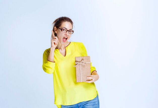 Mujer joven en camisa amarilla sosteniendo una caja de regalo de cartón