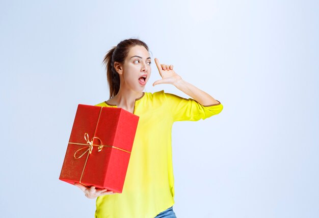 Mujer joven en camisa amarilla sosteniendo una caja de regalo roja dada en el día de San Valentín