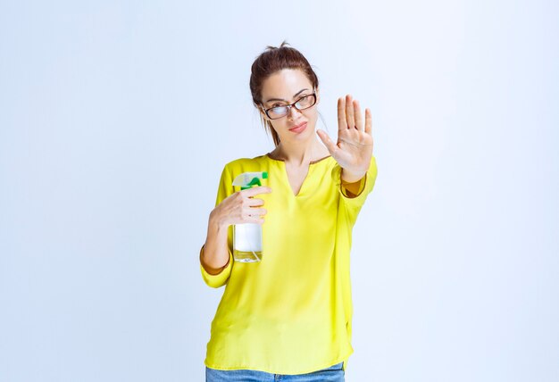 Mujer joven con camisa amarilla sosteniendo un spray de limpieza y negándose a compartir con nadie