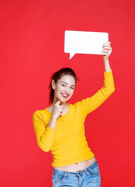 Mujer joven en camisa amarilla sosteniendo un tablero de información rectangular