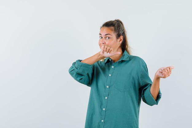 Mujer joven con camisa azul apuntando hacia atrás y mirando atenta