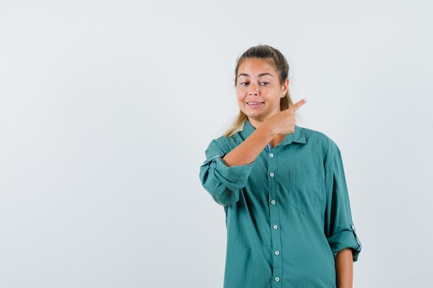 Mujer joven con camisa azul apuntando a un lado y mirando seguro