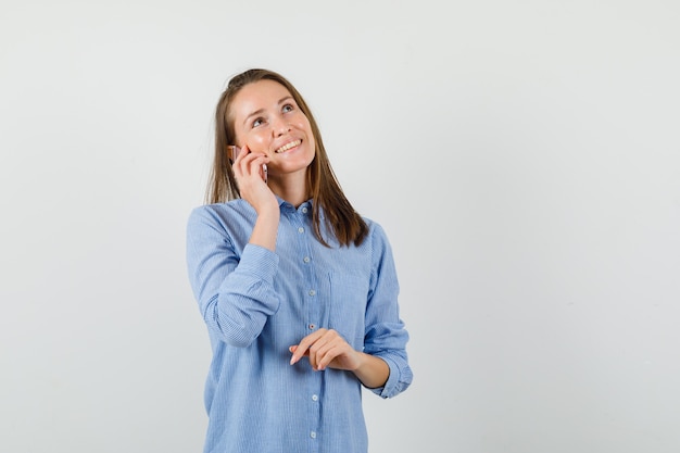 Mujer joven con camisa azul hablando por teléfono móvil y mirando esperanzado