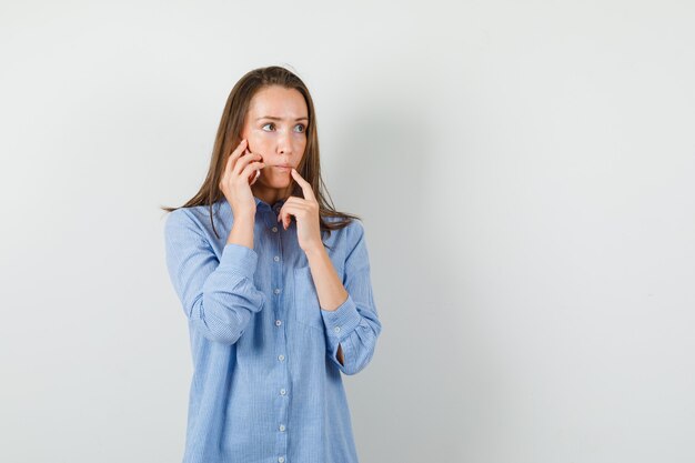 Mujer joven con camisa azul hablando por teléfono móvil y mirando pensativo