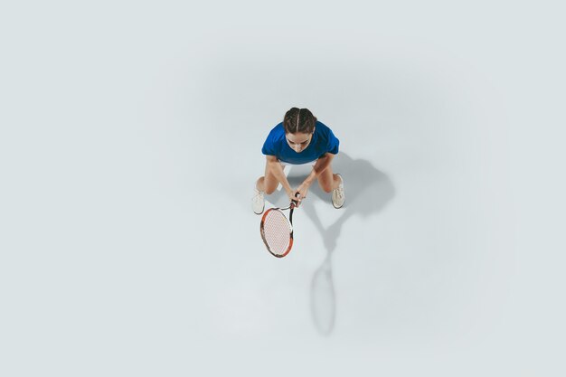 Mujer joven con camisa azul jugando al tenis. Golpea la pelota con una raqueta.