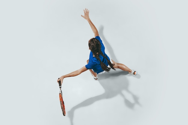 Mujer joven con camisa azul jugando al tenis. Golpea la pelota con una raqueta.