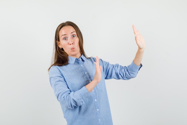 Foto gratuita mujer joven en camisa azul levantando las manos de manera preventiva y mirando asustada