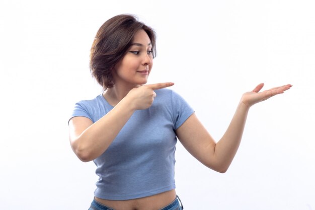 Mujer joven en camisa azul mostrando algo a un lado