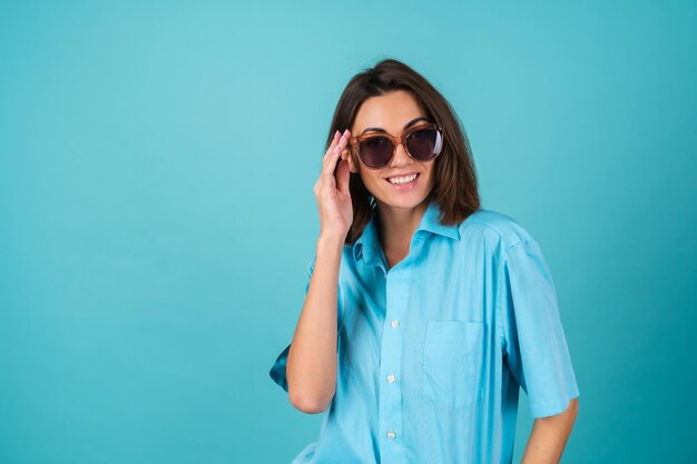 Mujer joven con una camisa azul en una pared con gafas de sol, posando con estilo de moda