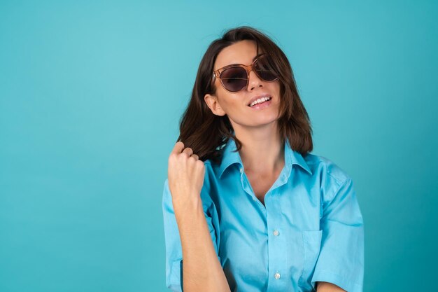 Mujer joven con una camisa azul en una pared con gafas de sol, posando con estilo de moda