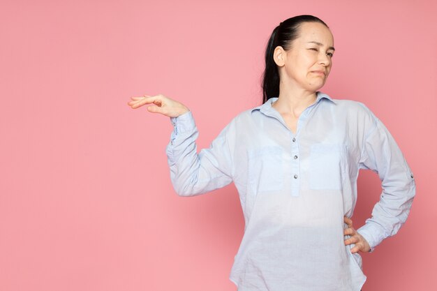 mujer joven en camisa azul posando en la pared rosa