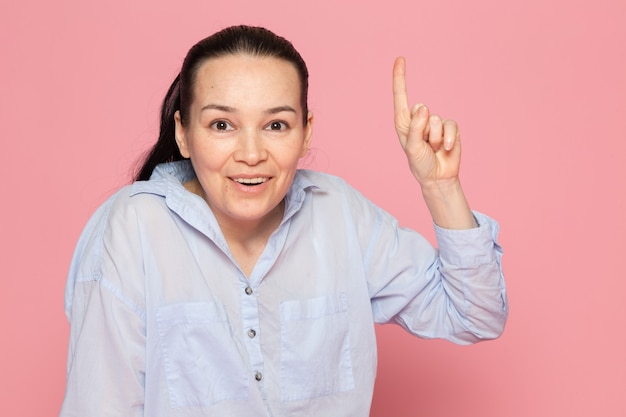 mujer joven en camisa azul posando en la pared rosa