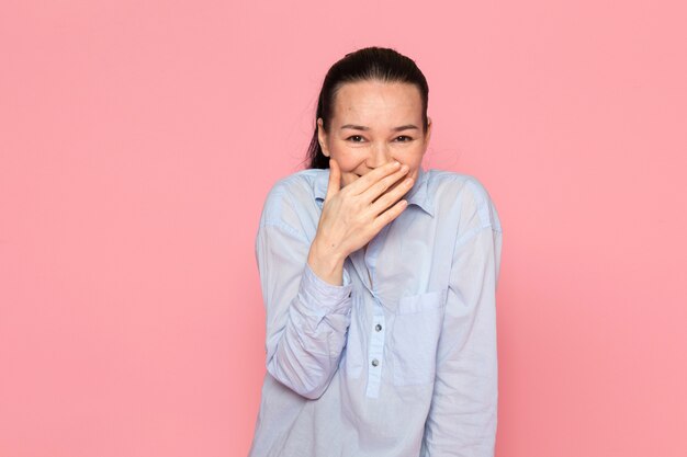 mujer joven en camisa azul posando en la pared rosa