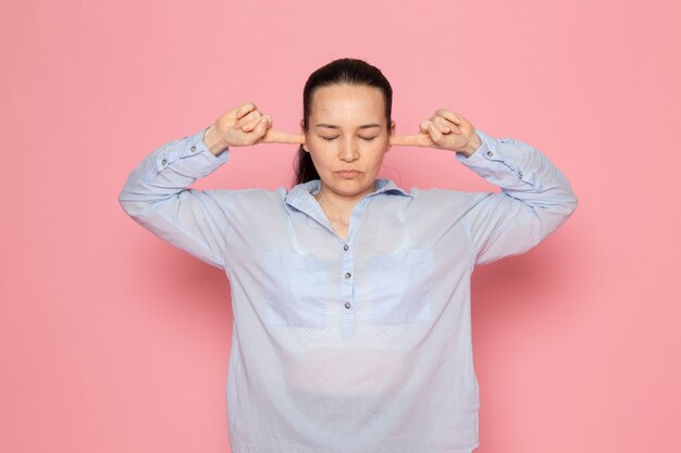 mujer joven en camisa azul posando en la pared rosa