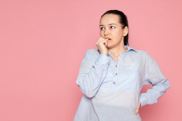 mujer joven en camisa azul posando en la pared rosa