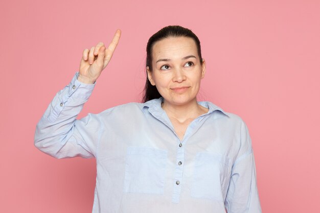 mujer joven en camisa azul posando en la pared rosa