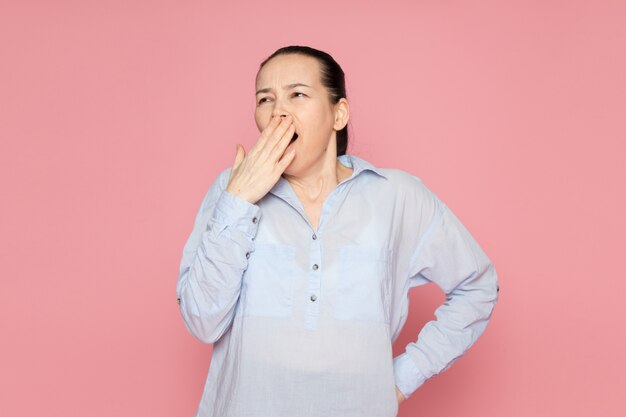 mujer joven en camisa azul posando en la pared rosa