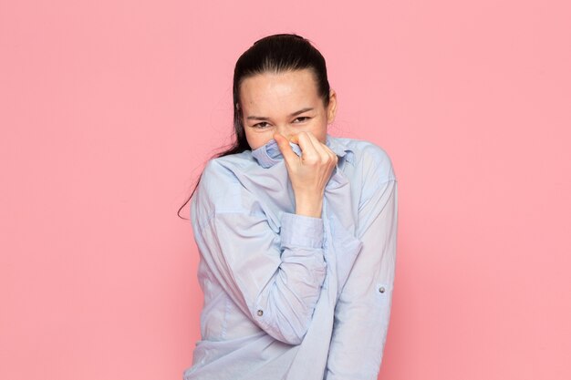 mujer joven en camisa azul posando en la pared rosa