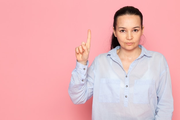 mujer joven en camisa azul posando en la pared rosa