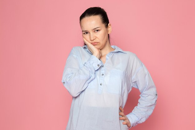 mujer joven en camisa azul posando en la pared rosa