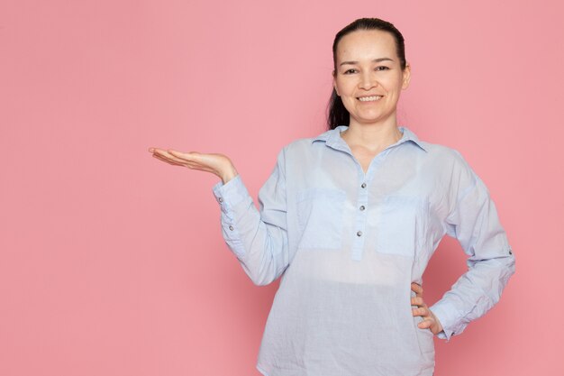 mujer joven en camisa azul sonriendo en la pared rosa