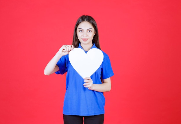 Mujer joven con camisa azul sosteniendo una figura de corazón blanco