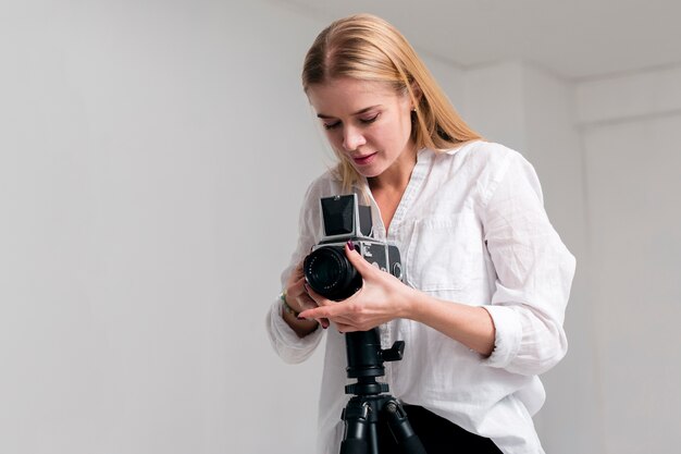 Mujer joven en camisa blanca ajustando la lente de la cámara