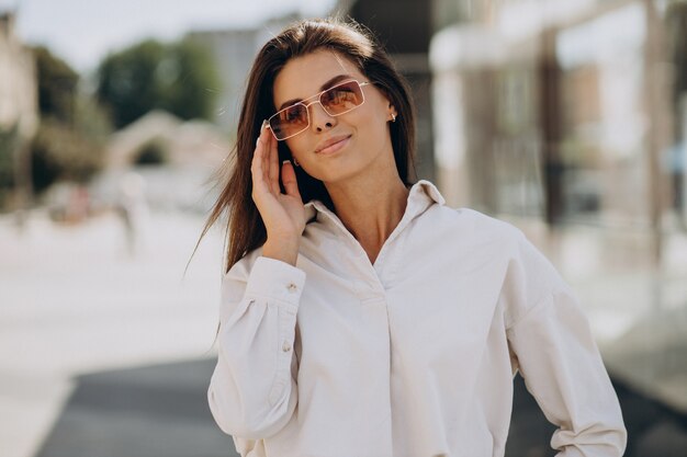 Mujer joven con camisa blanca caminando fuera de las calles de verano