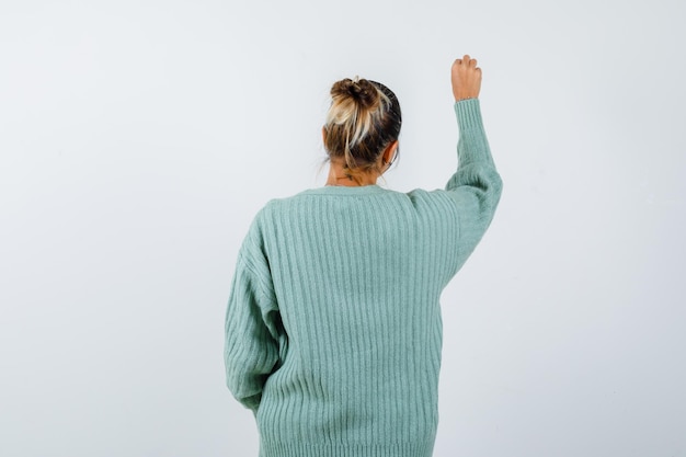 Foto gratuita mujer joven con camisa blanca y chaqueta de punto verde menta dando la vuelta y fingiendo escribir algo y mirando enfocado